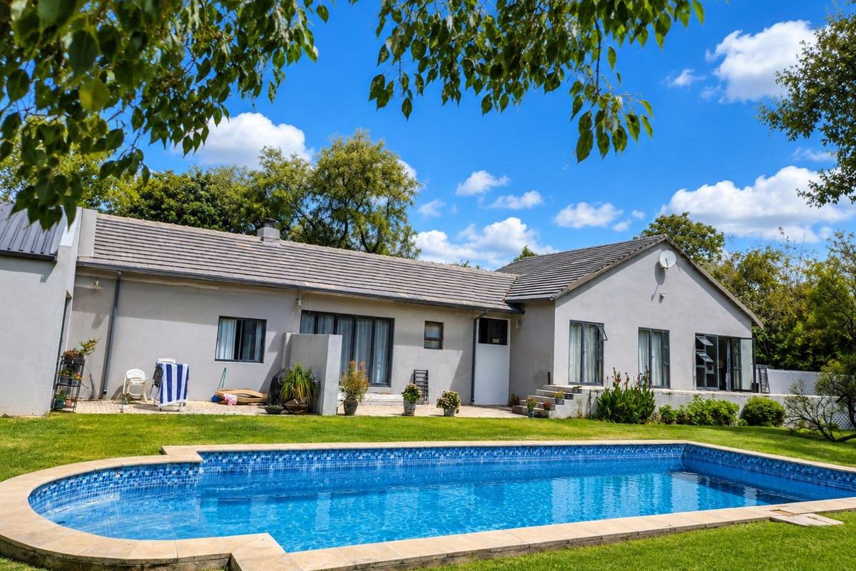 Rear view of the house featuring a swimming pool, paved patio area, and well-maintained garden space.