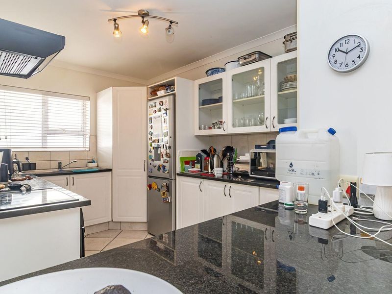 A functional kitchen featuring granite countertops, white cabinetry with glass-fronted display units, an extractor fan, and tiled flooring.