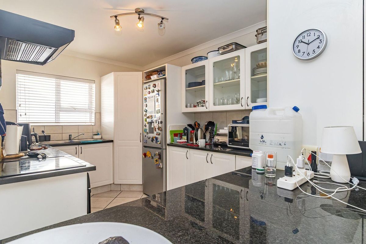 A functional kitchen featuring granite countertops, white cabinetry with glass-fronted display units, an extractor fan, and tiled flooring.