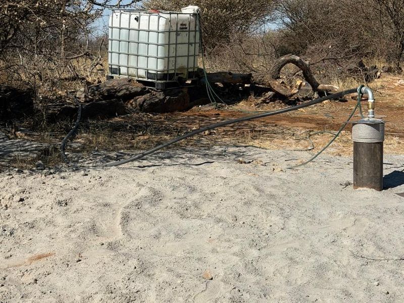 Agricultural land featuring a borehole with connected irrigation piping and a water storage tank situated in a natural bushveld setting.