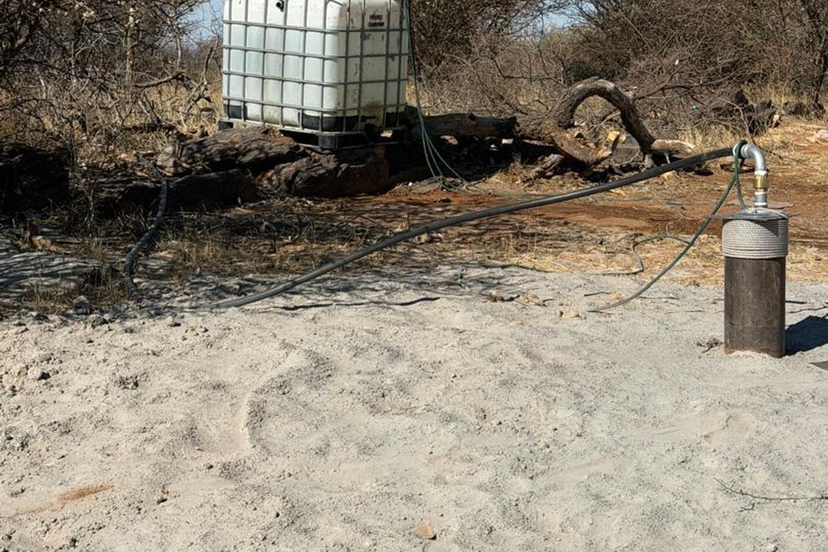 Agricultural land featuring a borehole with connected irrigation piping and a water storage tank situated in a natural bushveld setting.