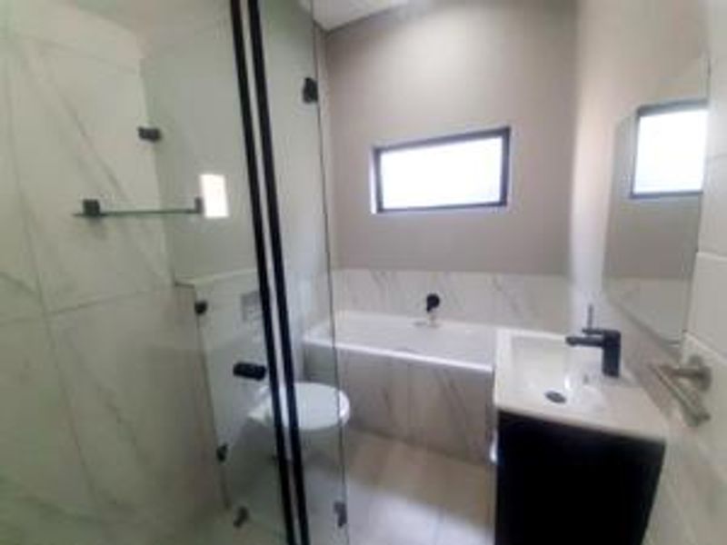 A modern bathroom featuring a glass shower enclosure, a built-in bathtub, a vanity basin, and contemporary black tapware with tiled finishes.