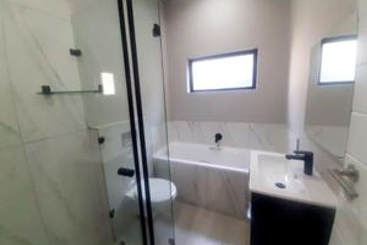 A modern bathroom featuring a glass shower enclosure, a built-in bathtub, a vanity basin, and contemporary black tapware with tiled finishes.