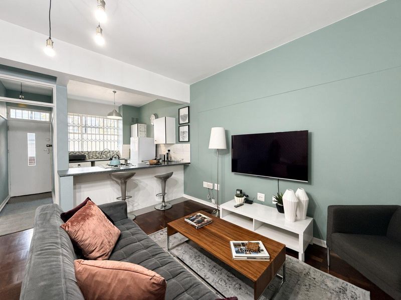 An open-plan living and kitchen area featuring a breakfast bar, modern cabinetry, and laminate flooring, creating a functional and well-lit living space.