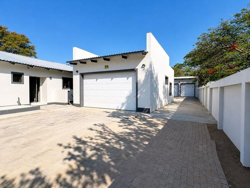 A well-maintained exterior view featuring a clean paved driveway leading to a modern garage with a white sectional door and boundary wall.