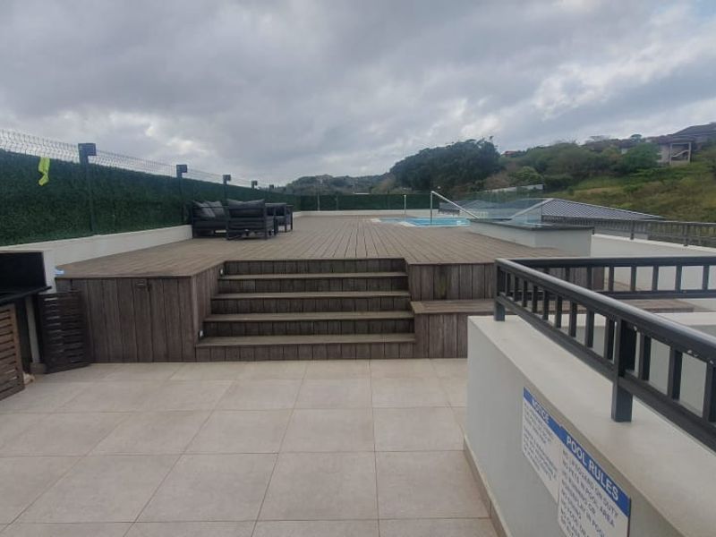 An elevated outdoor pool area featuring timber decking, a built-in outdoor kitchen counter with a sink, and panoramic views of the surrounding landscape.