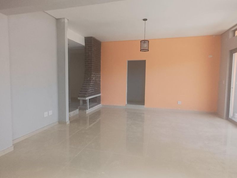 Spacious, empty living area featuring tiled flooring, a brick fireplace, and a sliding glass door leading to the exterior.