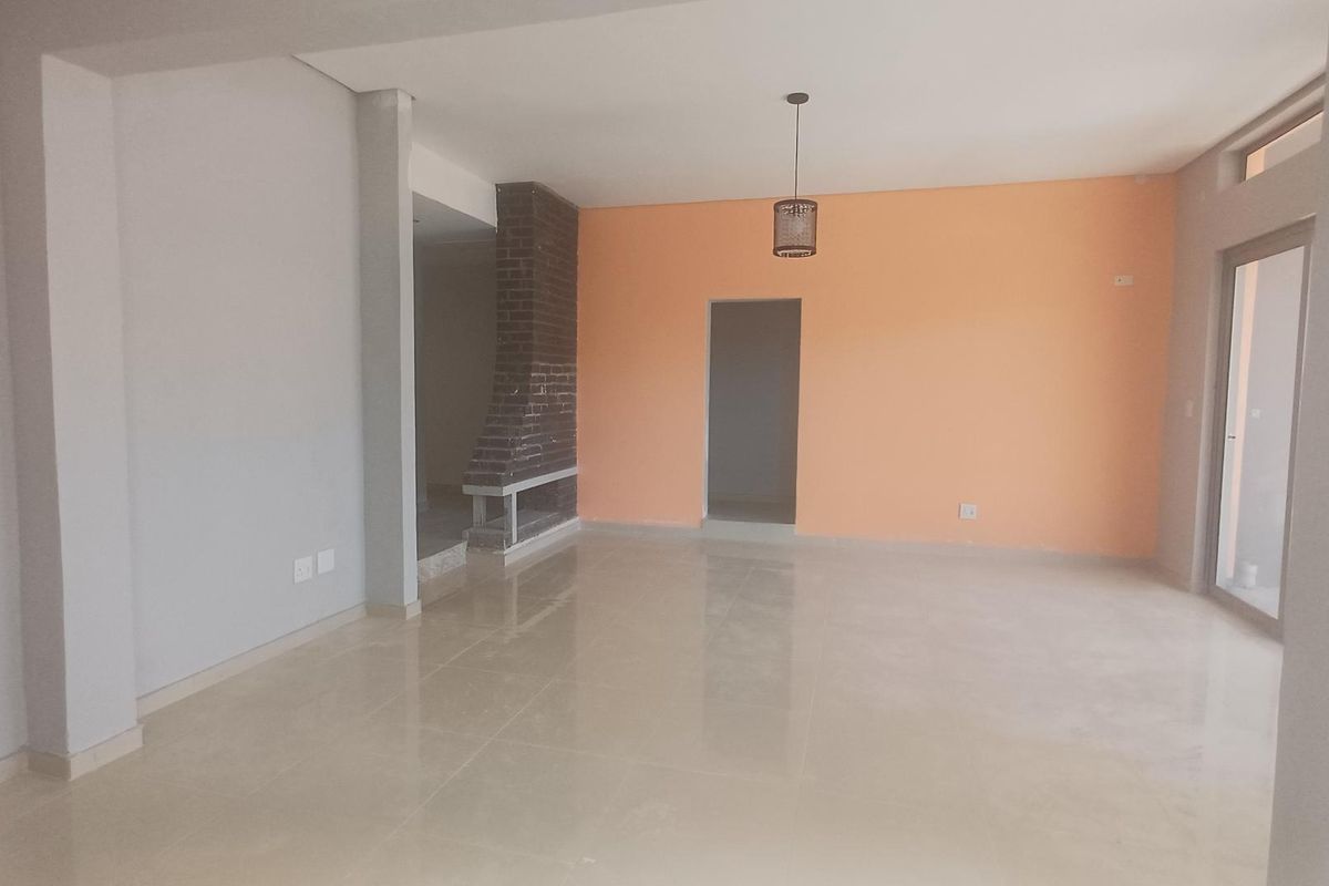 Spacious, empty living area featuring tiled flooring, a brick fireplace, and a sliding glass door leading to the exterior.