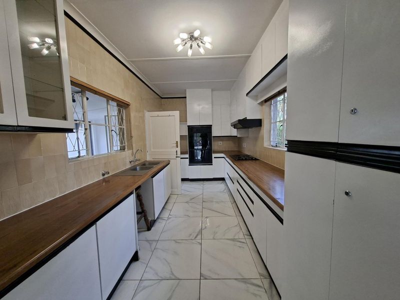 A clean, galley-style kitchen featuring white cabinetry, wooden countertops, built-in oven, gas hob, and modern tiled flooring.