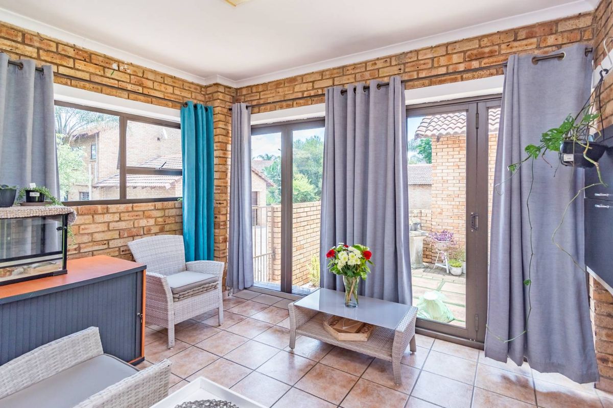 A bright living area featuring exposed brick walls, tiled flooring, and large aluminium sliding doors providing direct access to the rear patio.