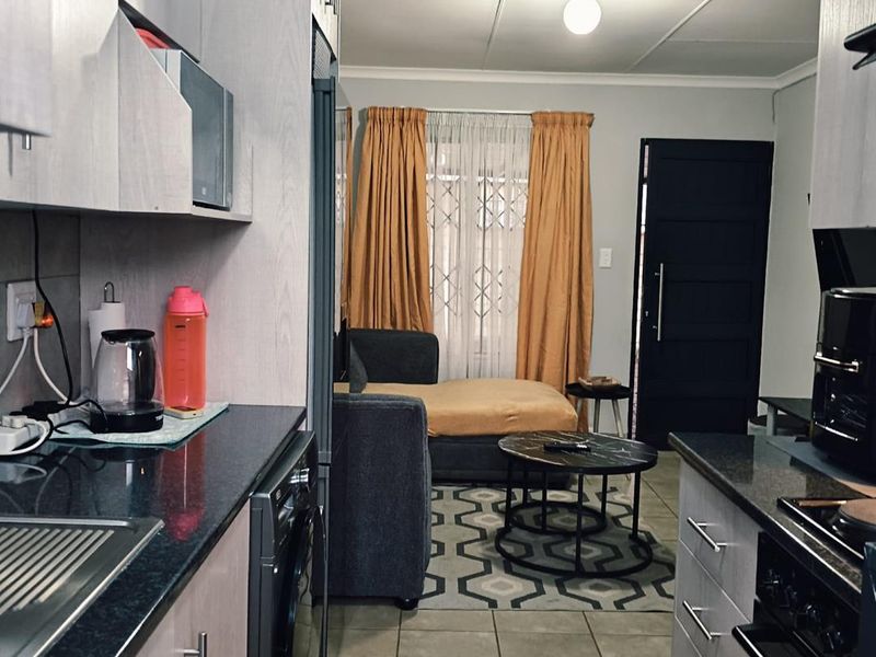 Open-plan kitchen and living area featuring modern cabinetry, granite countertops, tiled flooring, and direct access to the entrance.