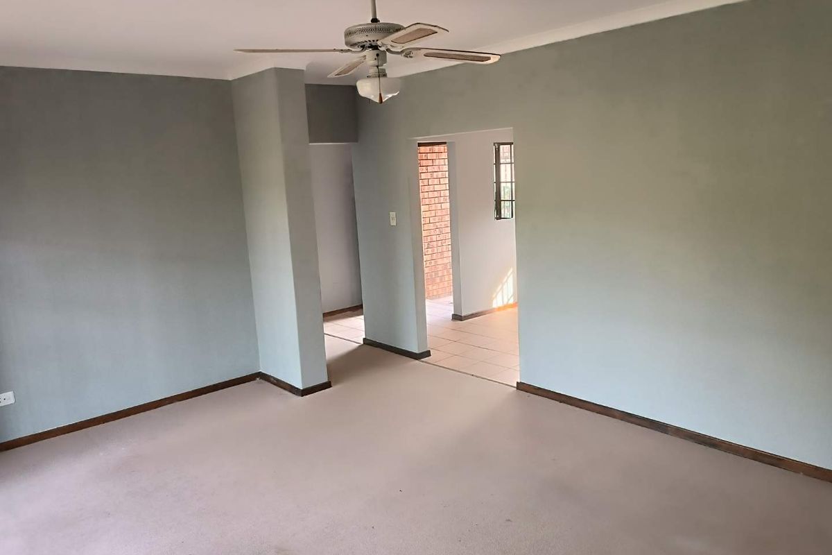 A spacious, empty living area featuring neutral wall tones, a ceiling fan, and direct access to an adjacent tiled room.
