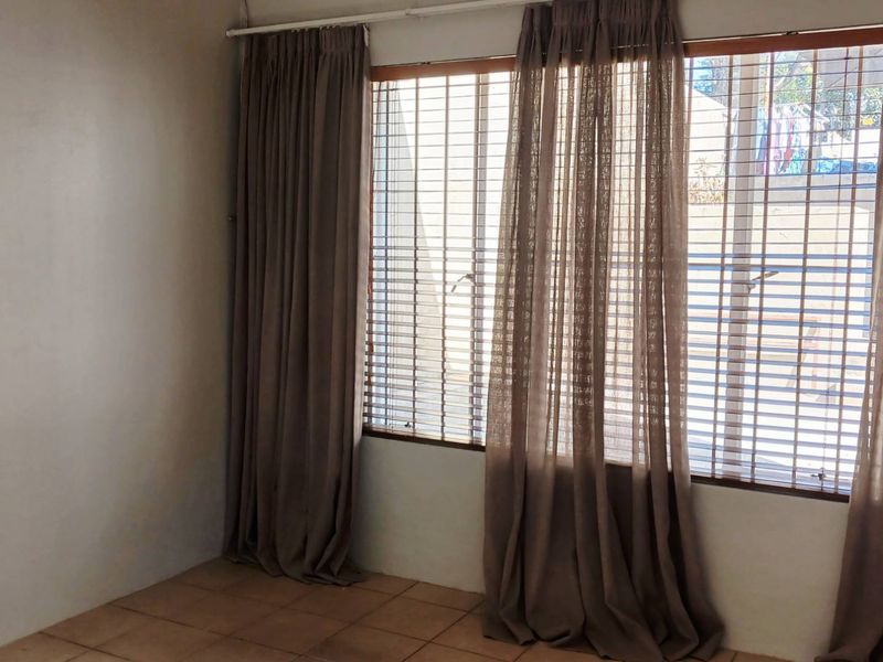 An empty living room featuring tiled flooring and large windows fitted with security bars and curtain tracks.