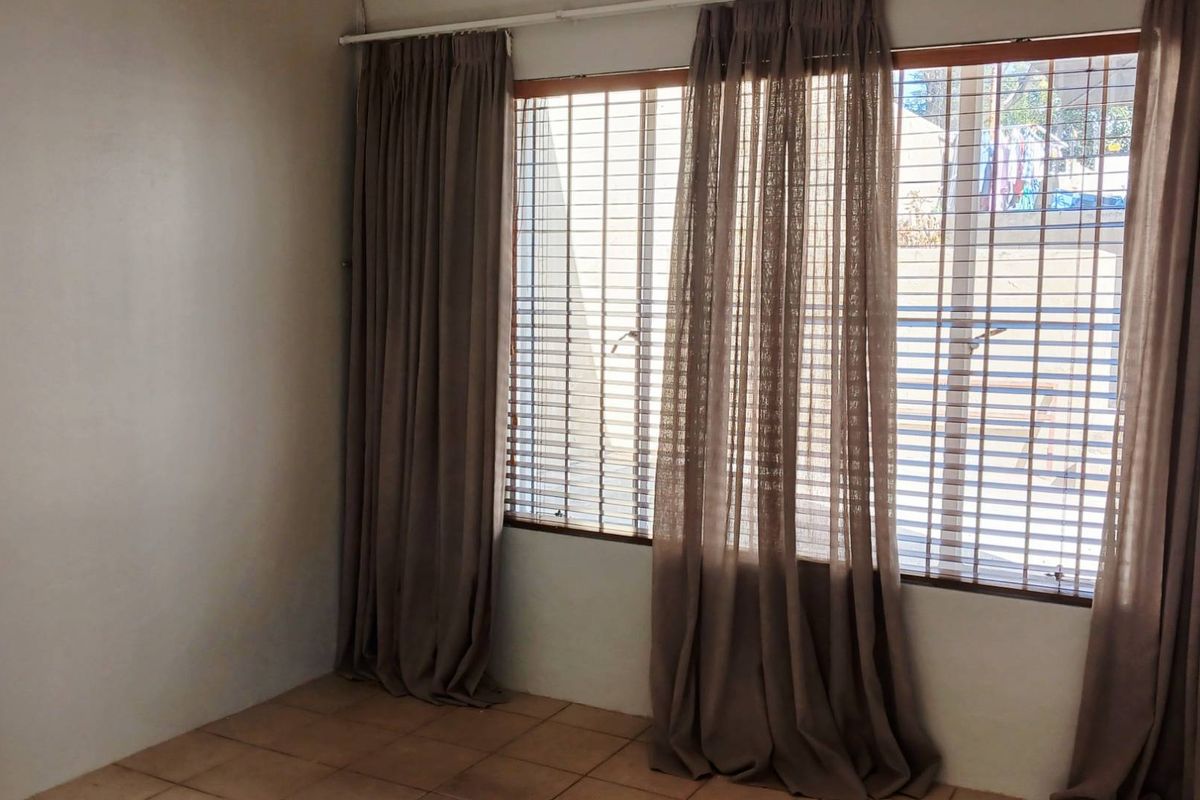 An empty living room featuring tiled flooring and large windows fitted with security bars and curtain tracks.