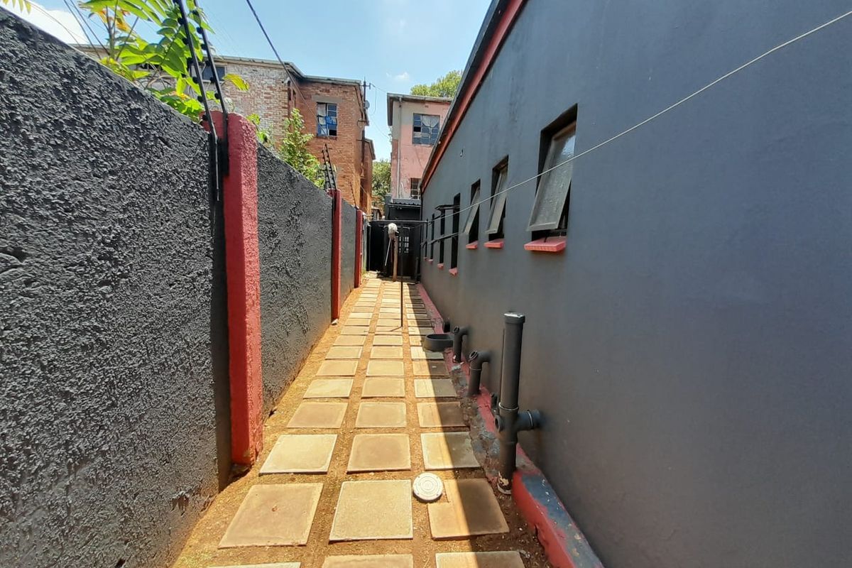 A narrow side passage featuring a paved walkway, boundary wall with electric fencing, and exterior wall access with exposed plumbing.