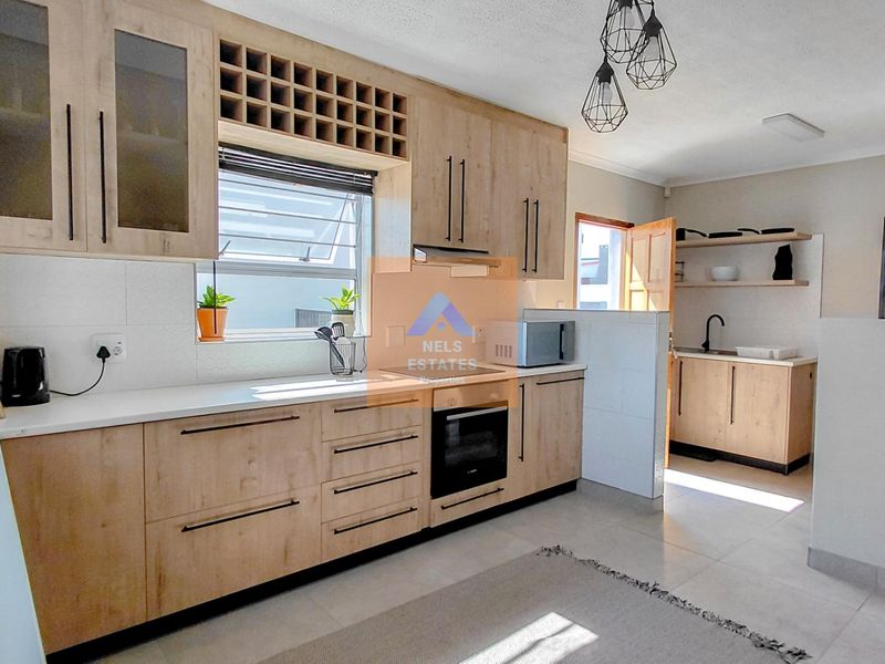 Modern kitchen featuring light wood-finish cabinetry, integrated oven and hob, ample counter space, and a separate scullery area with a sink.