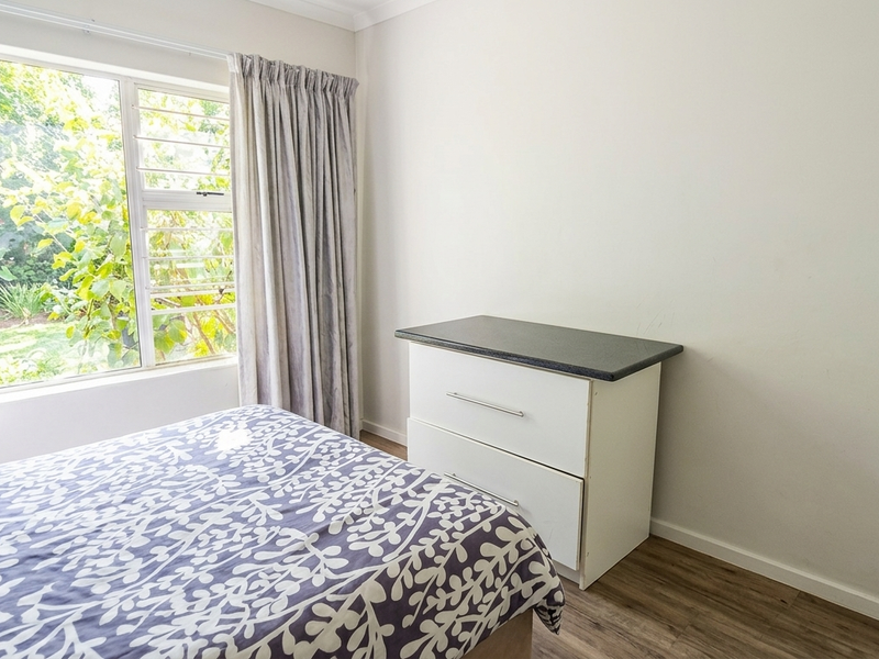 A bedroom featuring laminate flooring, neutral walls, and a large window with garden views, providing a bright and functional living space.