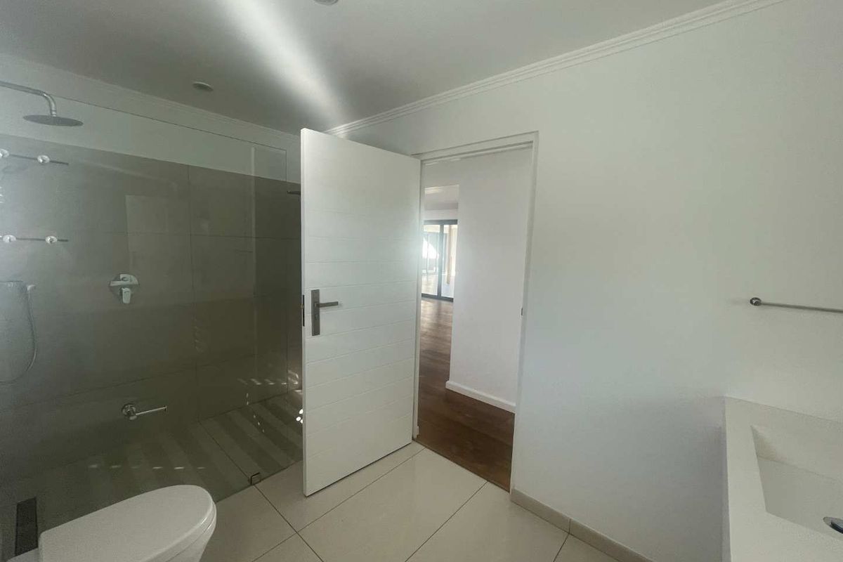 Modern bathroom featuring a walk-in shower with glass screen, wall-hung toilet, and vanity basin, finished with neutral floor tiles and recessed lighting.