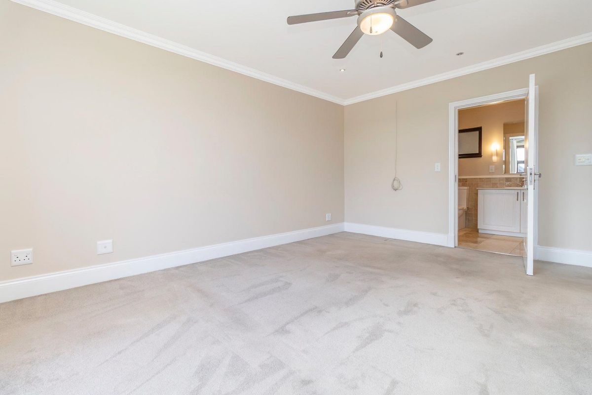 A spacious, carpeted bedroom featuring crown molding, a ceiling fan, and an en-suite bathroom with neutral finishes.