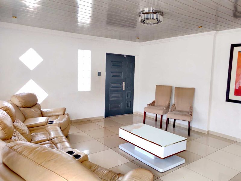 A living room featuring tiled flooring, a panelled ceiling, and decorative glass block windows, providing a bright and functional space.
