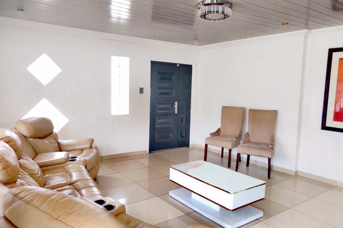 A living room featuring tiled flooring, a panelled ceiling, and decorative glass block windows, providing a bright and functional space.