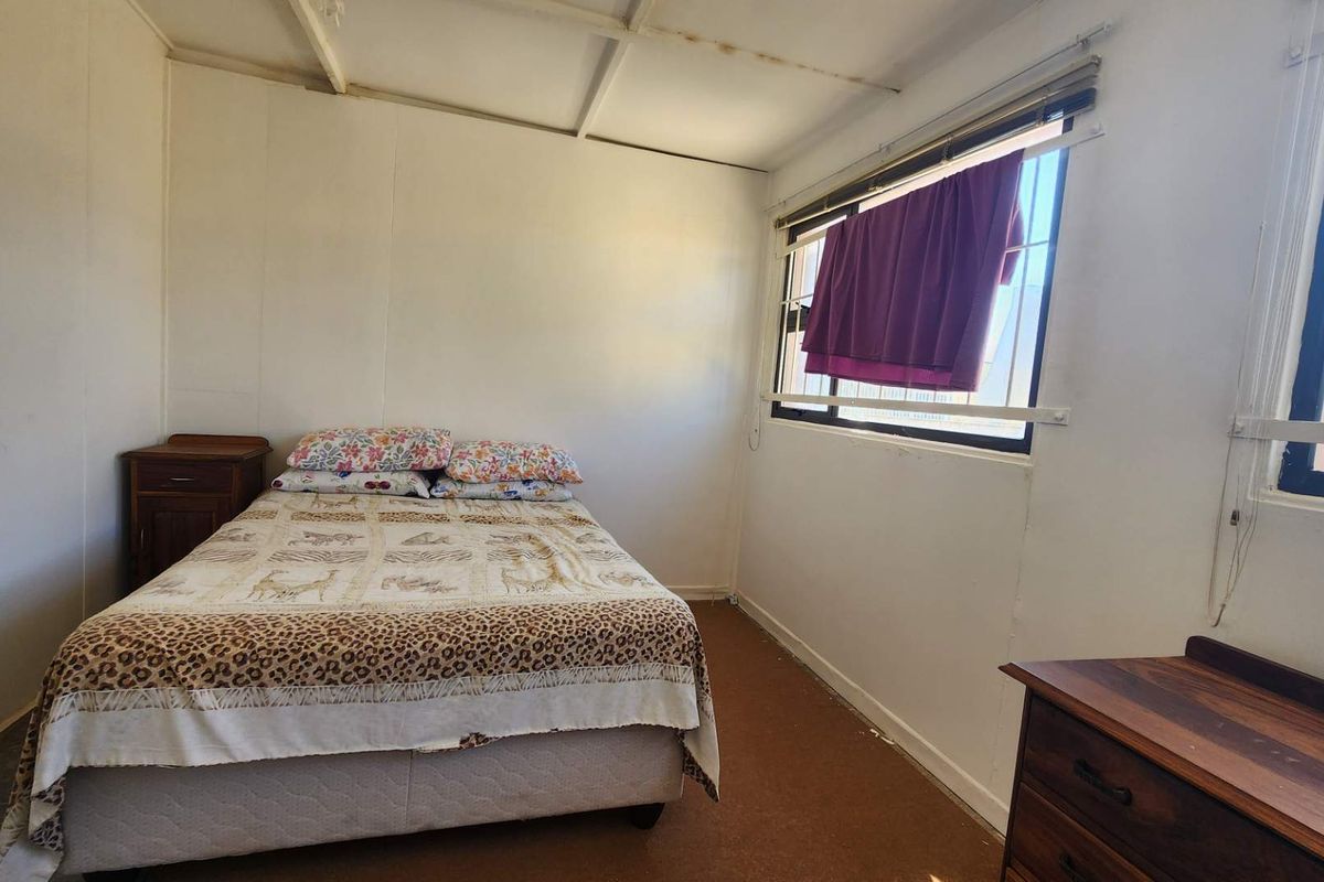A bedroom featuring exposed beam ceilings and aluminium window frames, requiring cosmetic updates to modernize the space.