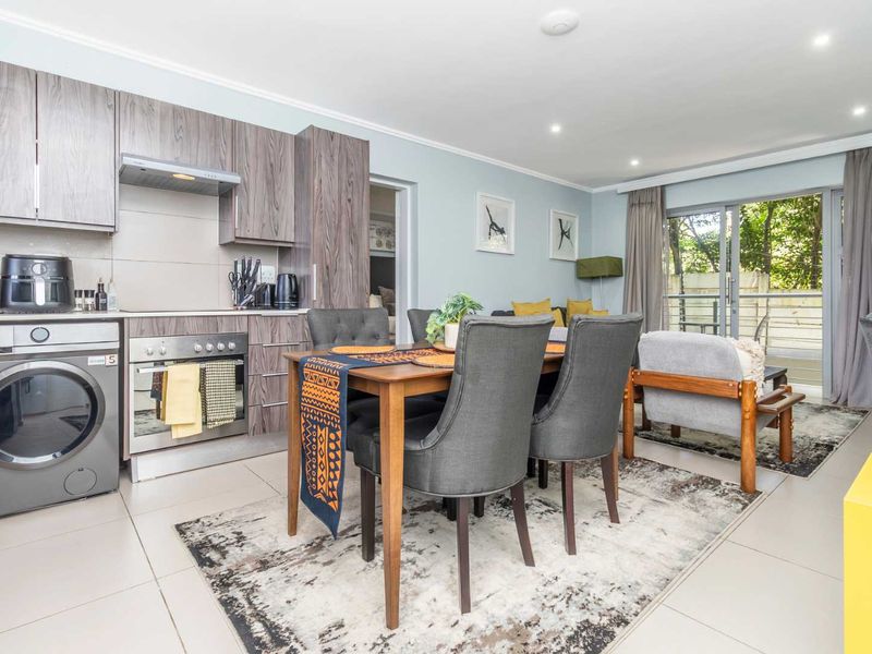 Open-plan living area featuring a modern kitchen with built-in cabinetry, integrated appliances, tiled flooring, and direct access to an outdoor balcony through sliding doors.