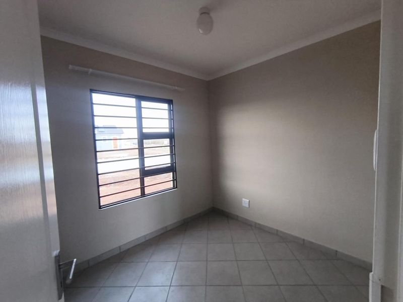 A clean, empty bedroom featuring neutral wall tones, tiled flooring, and a window fitted with security bars.