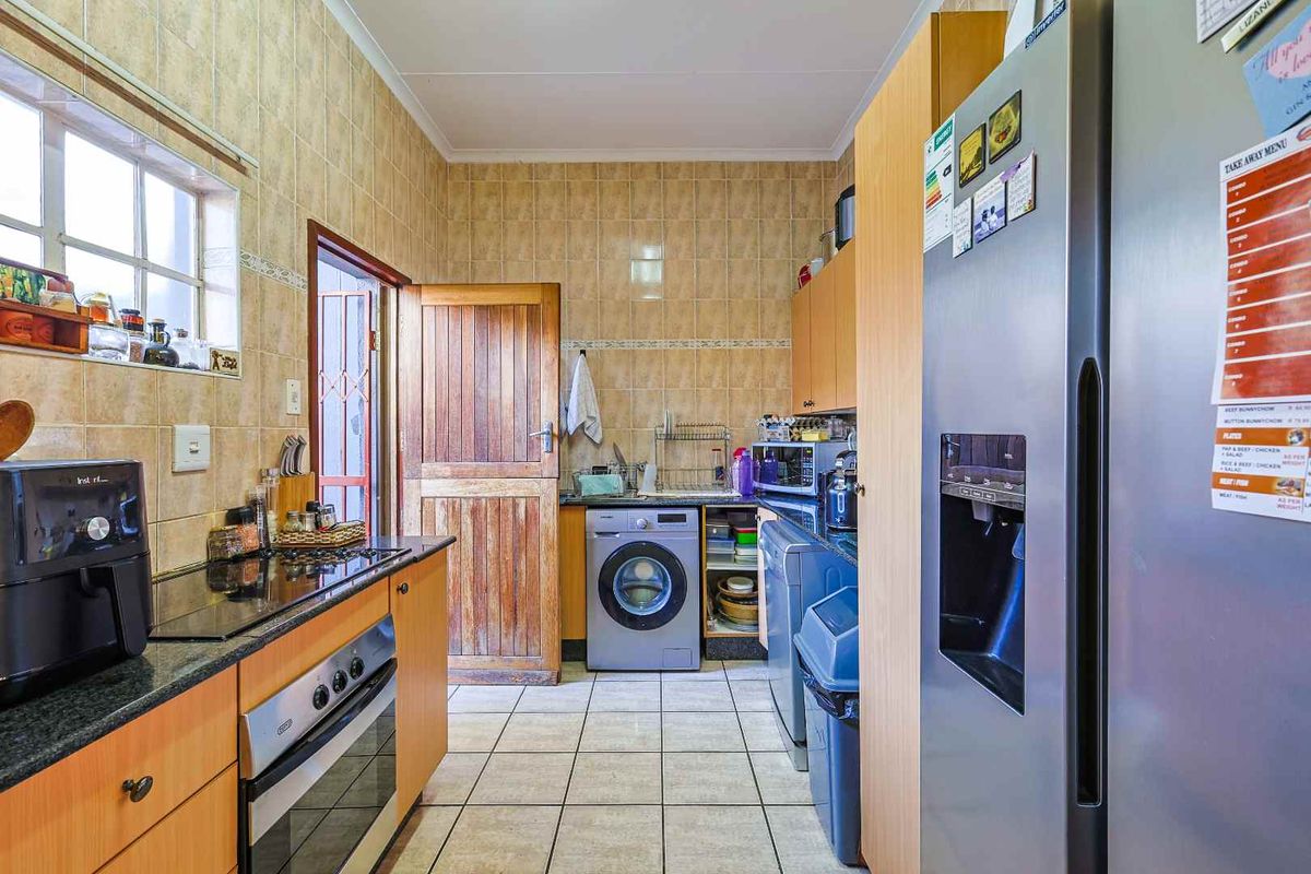 Functional kitchen featuring tiled walls, built-in cabinetry, integrated oven and hob, and dedicated space for laundry appliances.