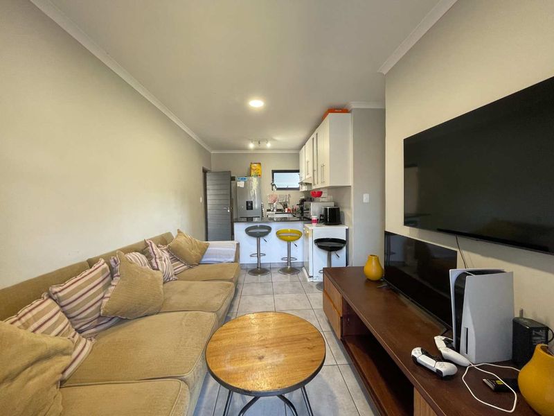 Open-plan living area featuring a compact kitchen with breakfast counter and tiled flooring, creating a functional combined living and dining space.