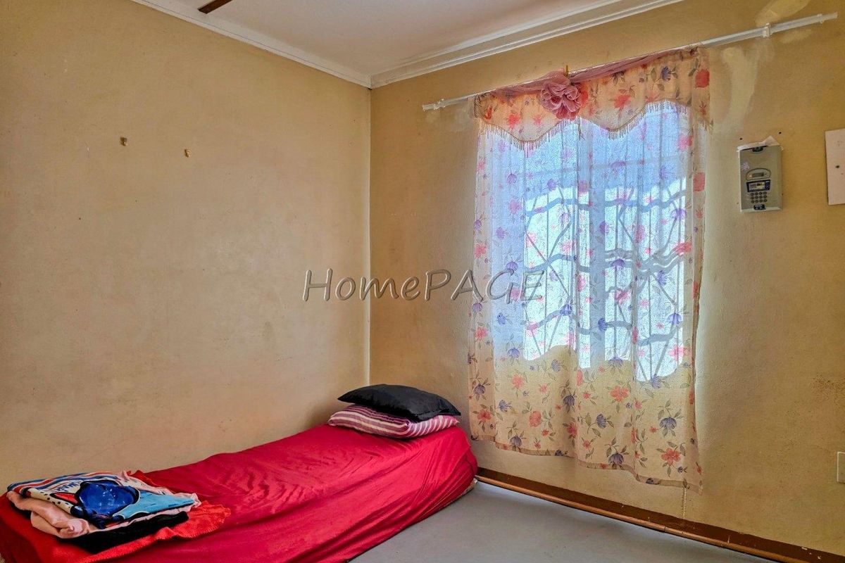 A bedroom featuring a window with security bars and basic wall finishes, requiring cosmetic updates and maintenance.