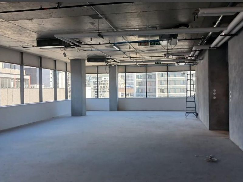 An expansive, open-plan commercial space featuring exposed industrial ceilings, concrete columns, and large windows providing ample natural light and urban views.