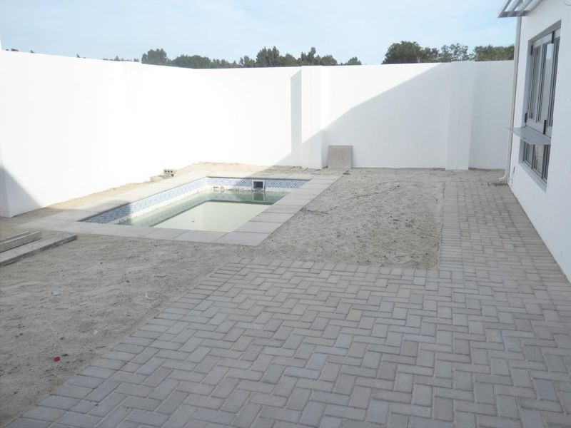 Outdoor pool area featuring a small swimming pool, paved patio section, and high boundary walls, currently awaiting final landscaping and garden completion.