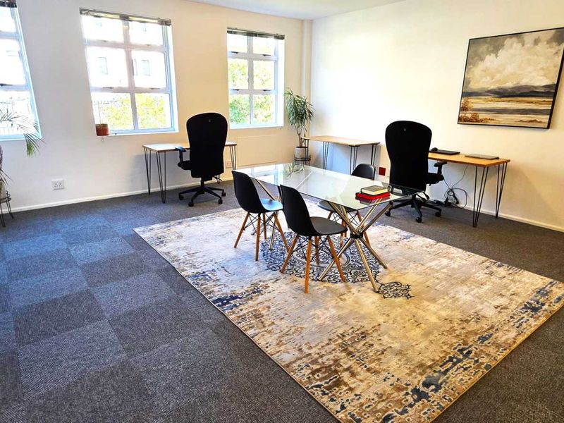 A bright, open-plan office space featuring large grid-pattern windows, neutral walls, and durable carpet tile flooring, suitable for a professional work environment.
