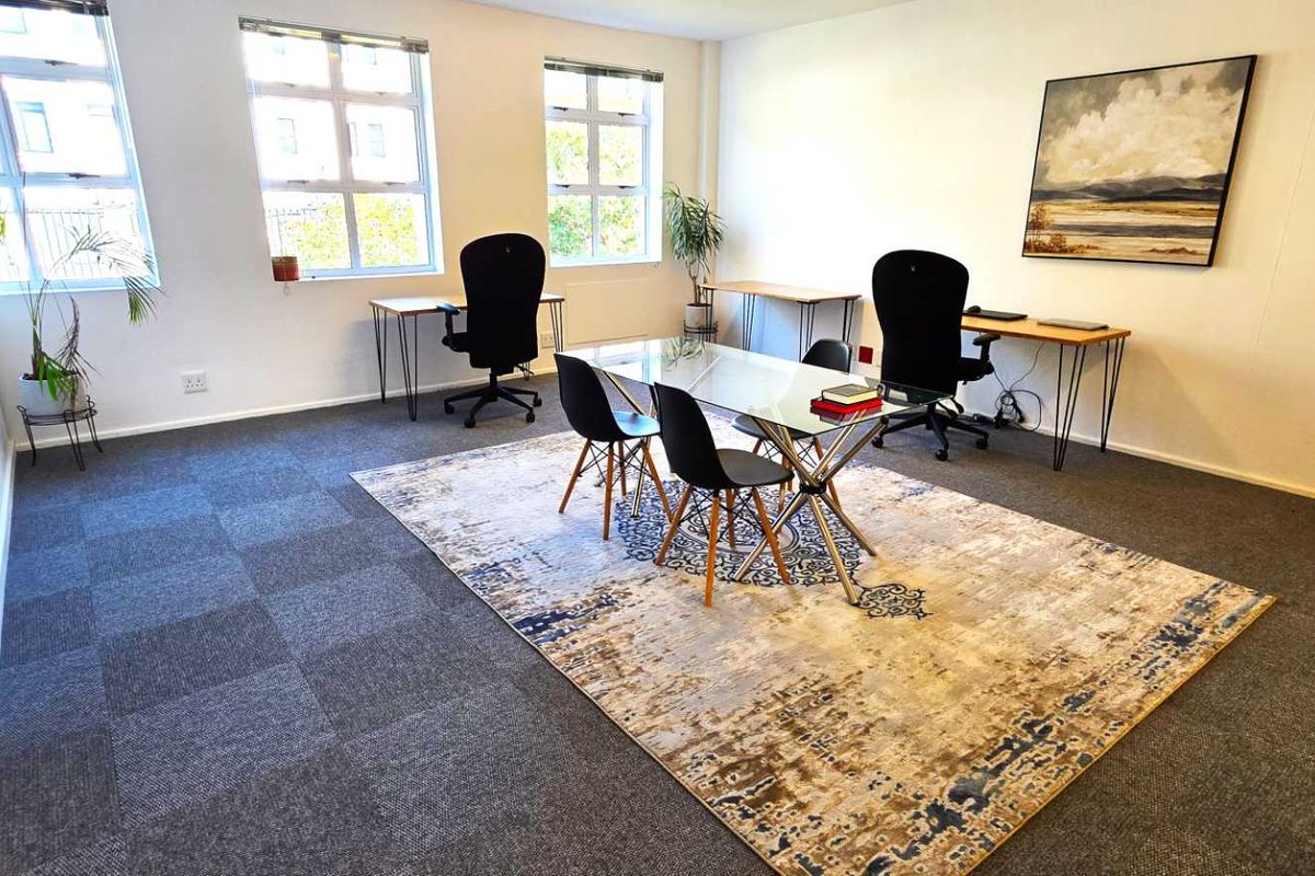 A bright, open-plan office space featuring large grid-pattern windows, neutral walls, and durable carpet tile flooring, suitable for a professional work environment.