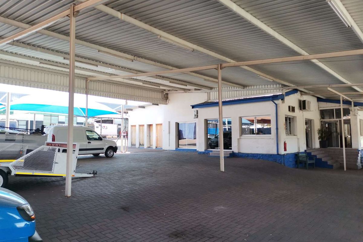 A large covered outdoor business area featuring extensive steel roofing, paved flooring, and multiple access points to the main building structure.