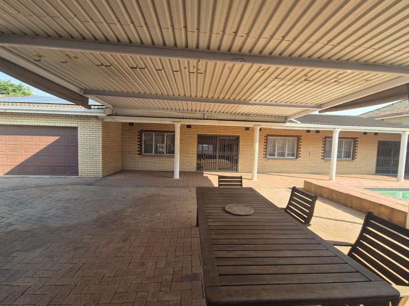 Spacious covered patio area featuring brick paving, a corrugated metal roof, and direct access to the swimming pool and garage.