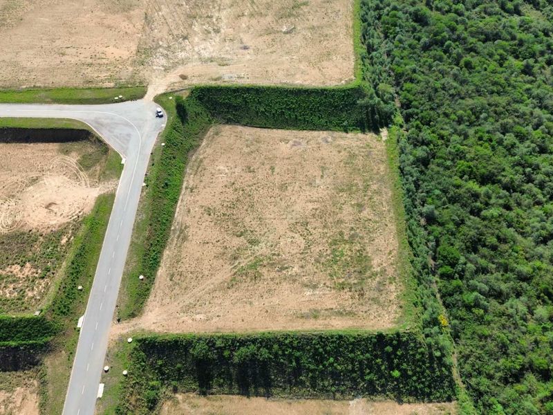Aerial view of a cleared industrial land parcel featuring paved road access and established perimeter embankments adjacent to a wooded area.