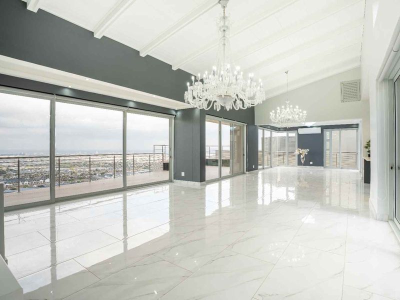 Spacious, light-filled living area featuring high vaulted ceilings, polished marble flooring, and expansive sliding glass doors opening to a panoramic balcony view.
