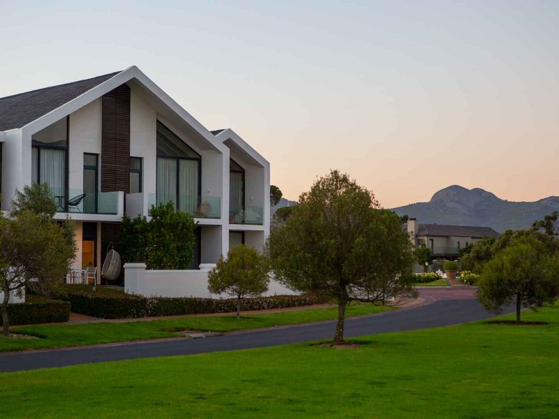 A modern apartment building with a pitched roof, glass balconies, and landscaped surroundings, set against a scenic mountain backdrop.