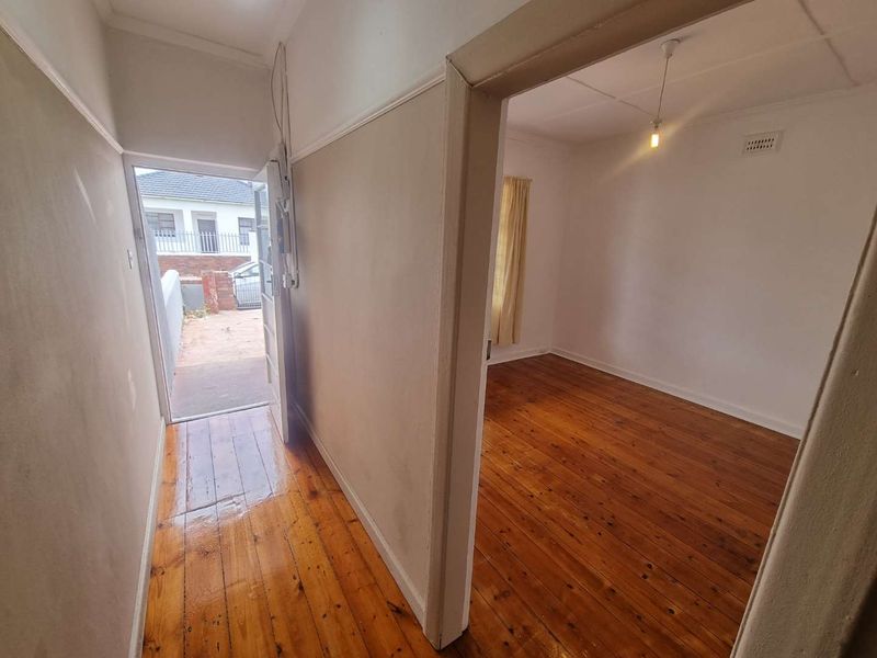 A bright hallway featuring polished hardwood flooring and direct access to the exterior, leading into an adjacent empty room.