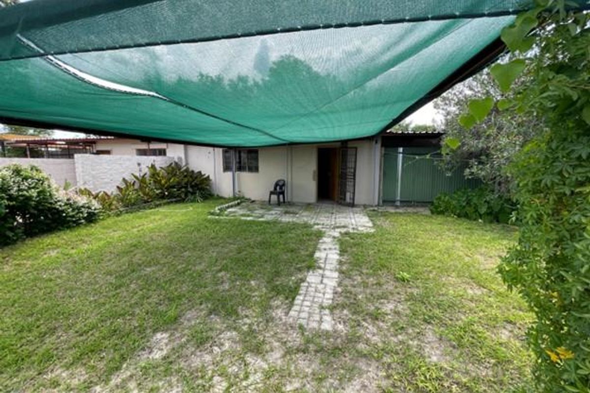 A rear garden area featuring a paved walkway, lawn, and a large green shade cloth canopy providing cover for the outdoor space.
