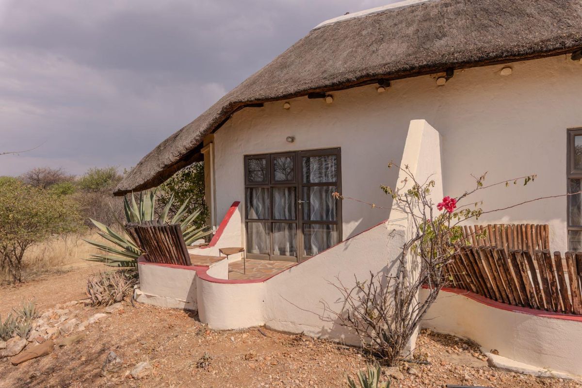 A rustic lodge unit featuring a traditional thatched roof, a private patio area with low masonry walls, and glass sliding door access.