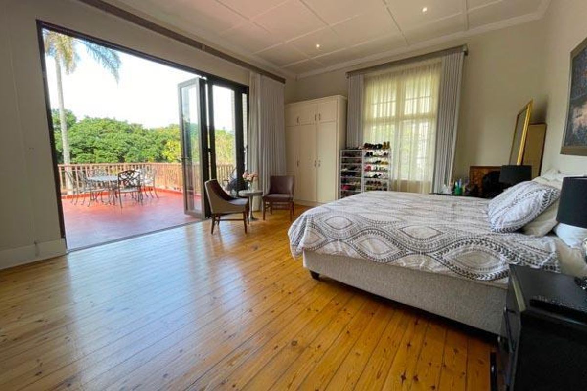 Spacious bedroom featuring polished timber flooring, built-in cabinetry, and large glass doors opening onto a private balcony with outdoor seating.