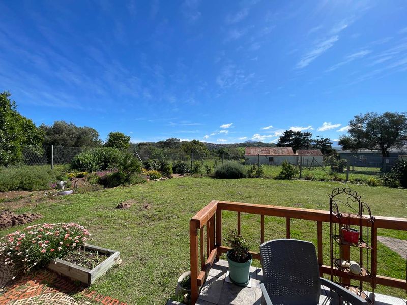 A spacious backyard garden featuring a timber balustrade deck, established lawn, and perimeter fencing with distant rural views.