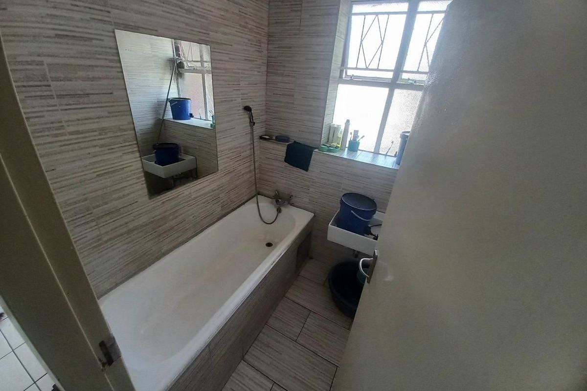 A functional bathroom featuring tiled walls and flooring, a built-in bathtub with a handheld shower attachment, and a wall-mounted basin.