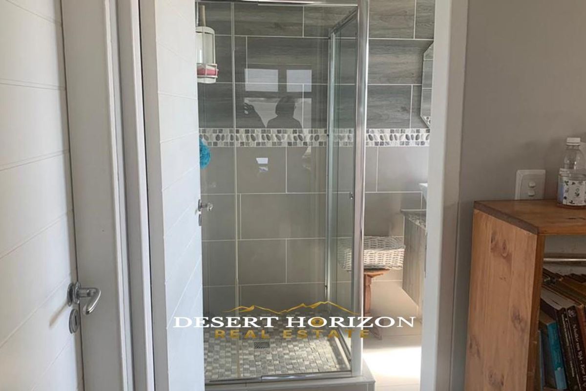A modern bathroom featuring a glass-enclosed shower with grey tiled walls and a mosaic-tiled shower floor.