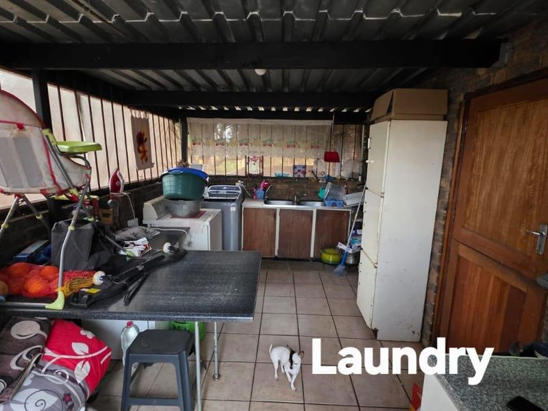 A functional laundry area featuring a double basin sink, built-in cabinetry, and tiled flooring under a corrugated metal roof structure.