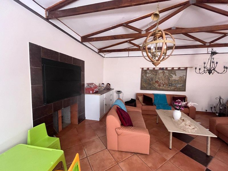 Spacious living room featuring exposed timber ceiling beams, terracotta-style tiled flooring, and a built-in fireplace with a dark tiled surround.