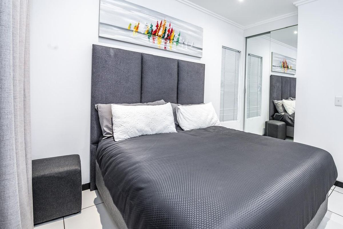 A well-maintained bedroom featuring tiled flooring, mirrored built-in wardrobes, and modern recessed ceiling lighting.